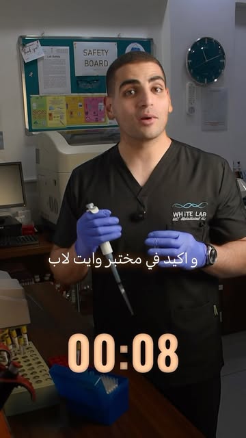 فني من وايت لاب يمسك ماصّة داخل المختبر أمام لوحة السلامة